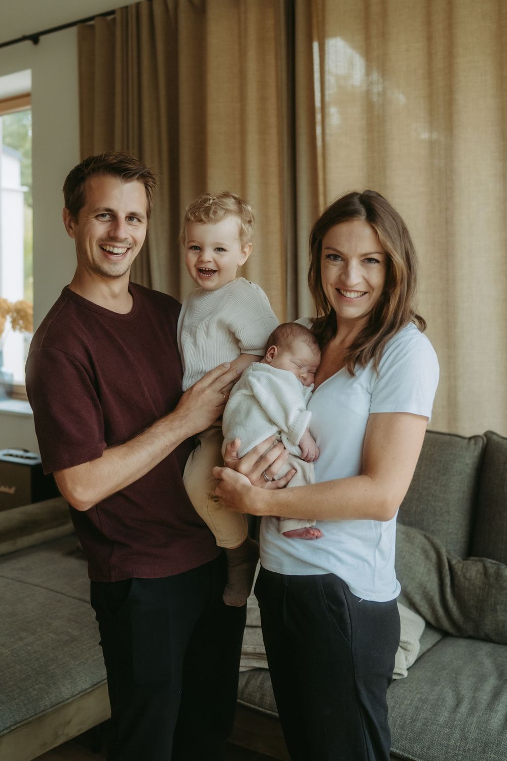 Happy young family with toddler and newborn baby posing together in cozy living room.