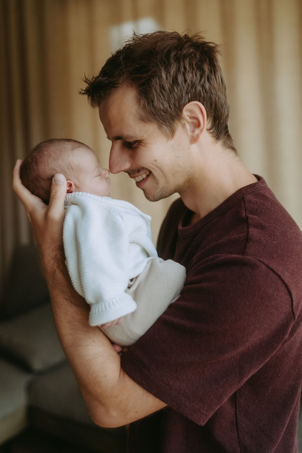 Smiling father holding his newborn baby face-to-face in a warm indoor setting.