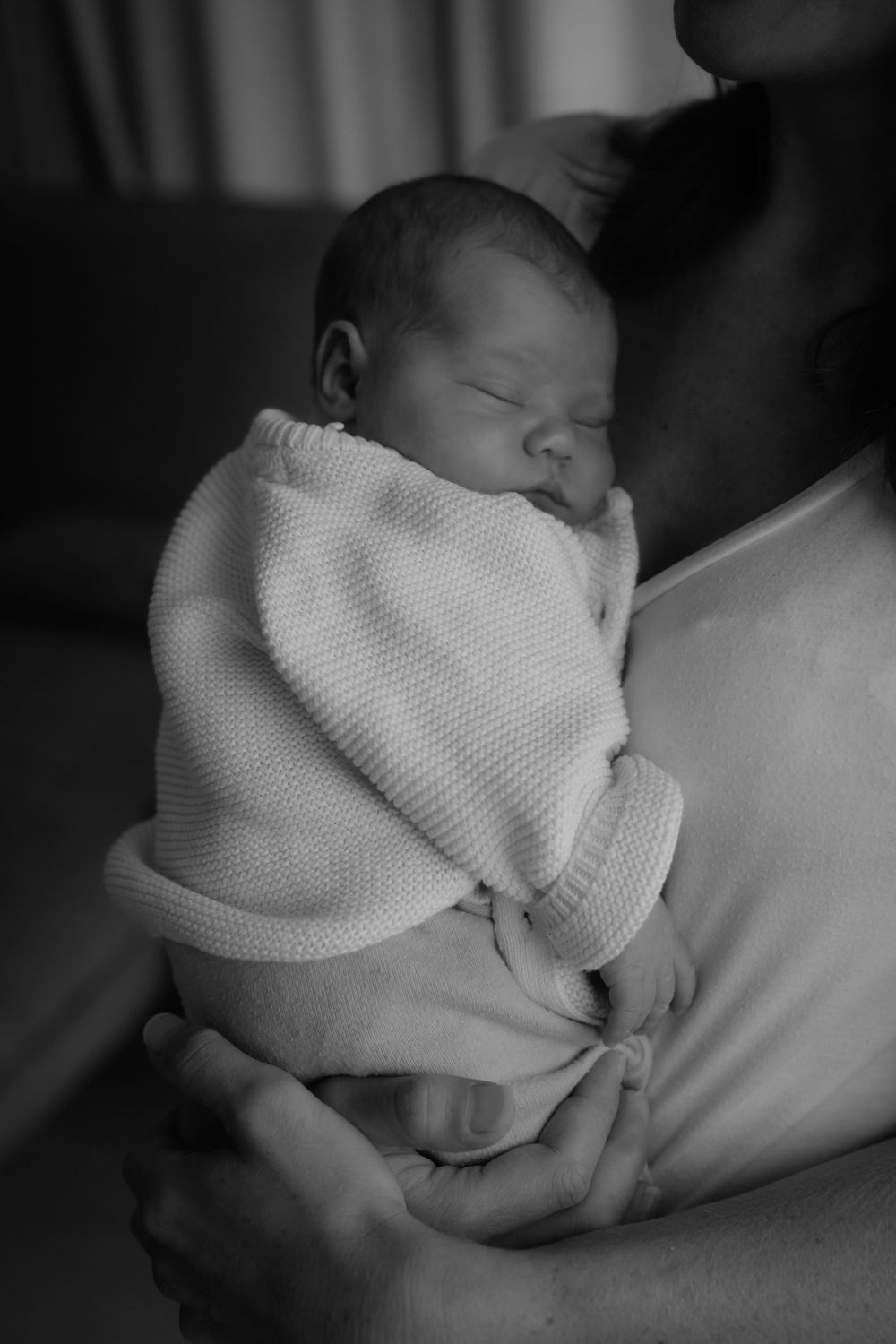 Black and white photo of a sleeping newborn baby wrapped in a knit blanket being held by a parent.