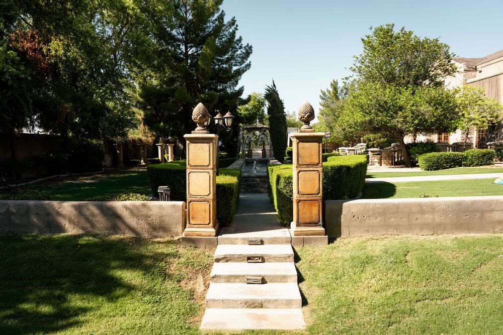 Elegant garden gate with ornate stone pillars and pine cone finials leading to a manicured green pathway.