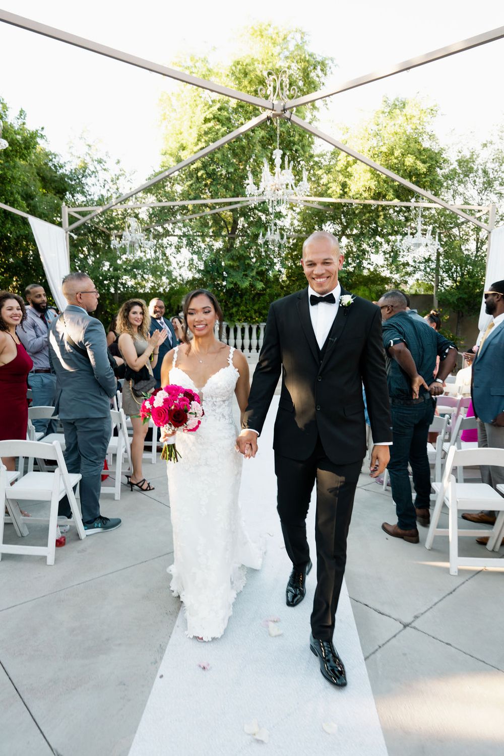 Newlyweds walk down aisle hand-in-hand as guests celebrate their outdoor wedding ceremony.