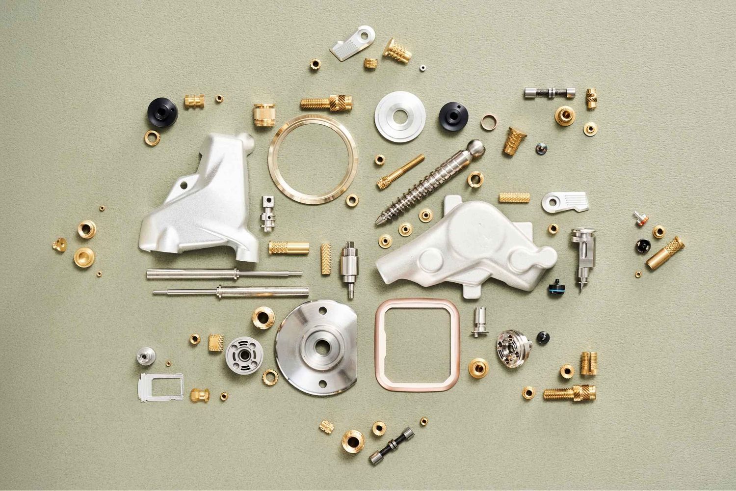 Assorted brass and metal mechanical parts, screws, fittings, and components arranged flat lay on a gray background.