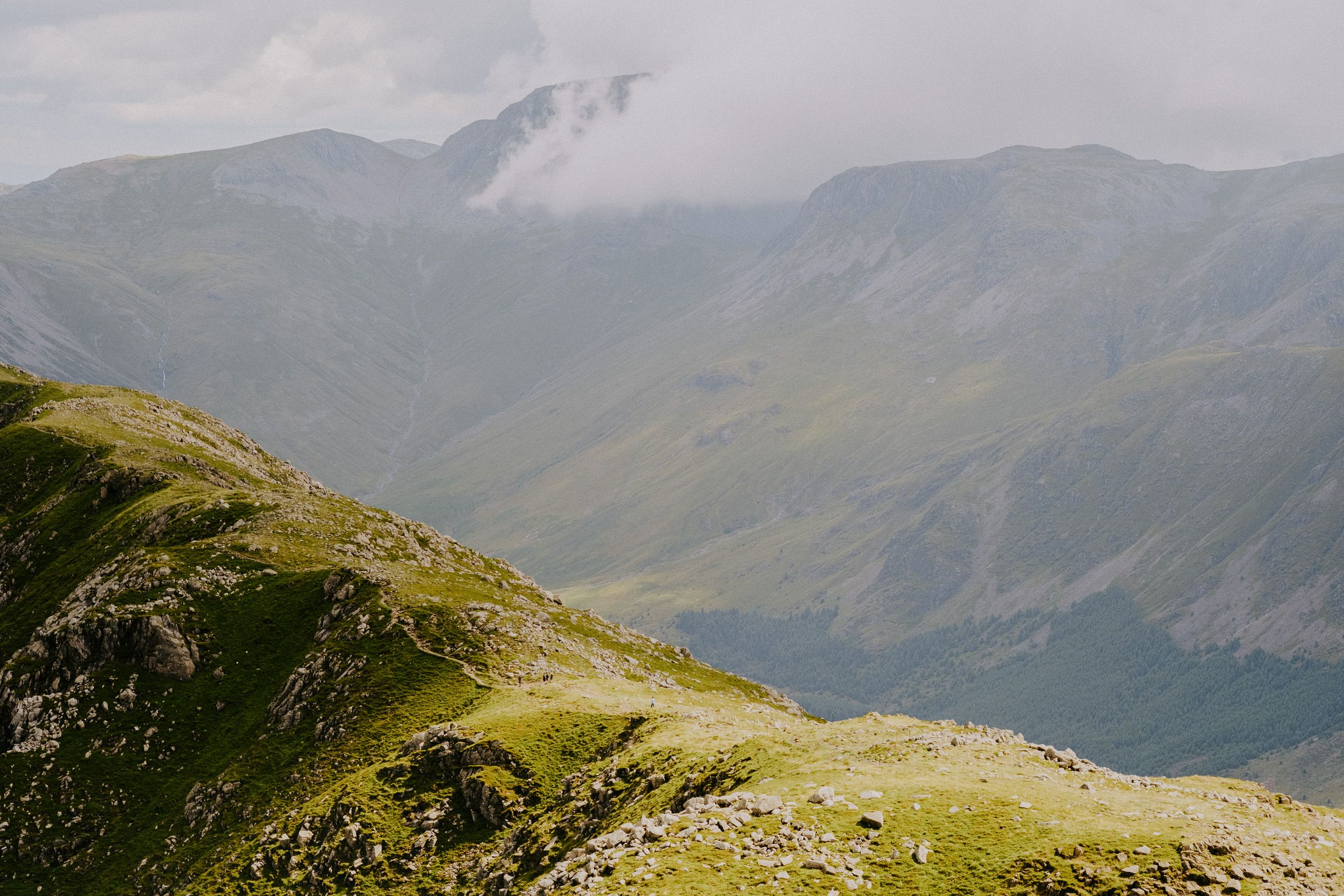 Lush green mountain ridge with dramatic valley views and misty peaks under cloudy skies in a scenic highland landscape.