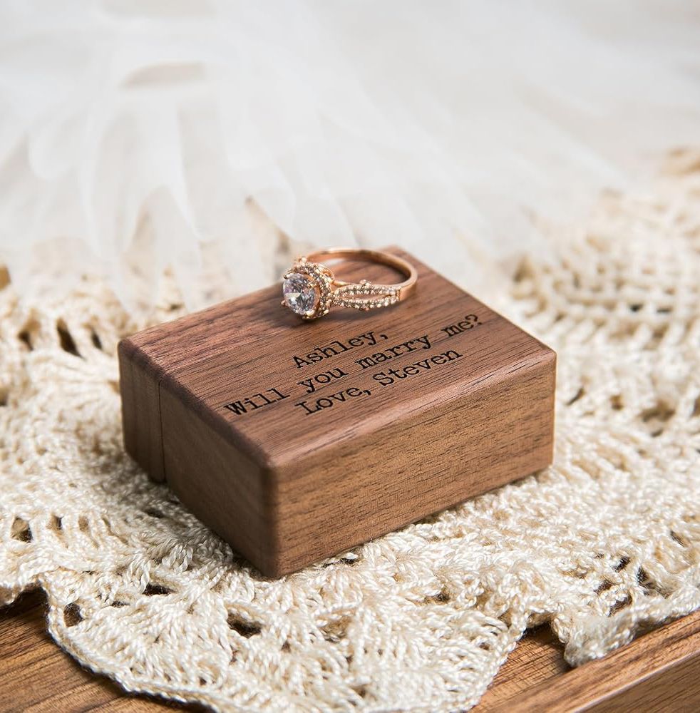 A ring box with a spotlight shining on a diamond ring, displayed next to a mini Eiffel Tower and coral roses.