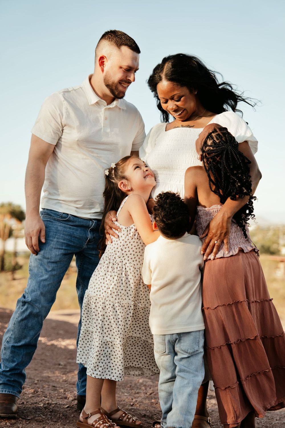 Happy interracial family with two young children embracing outdoors in a sunny desert landscape.