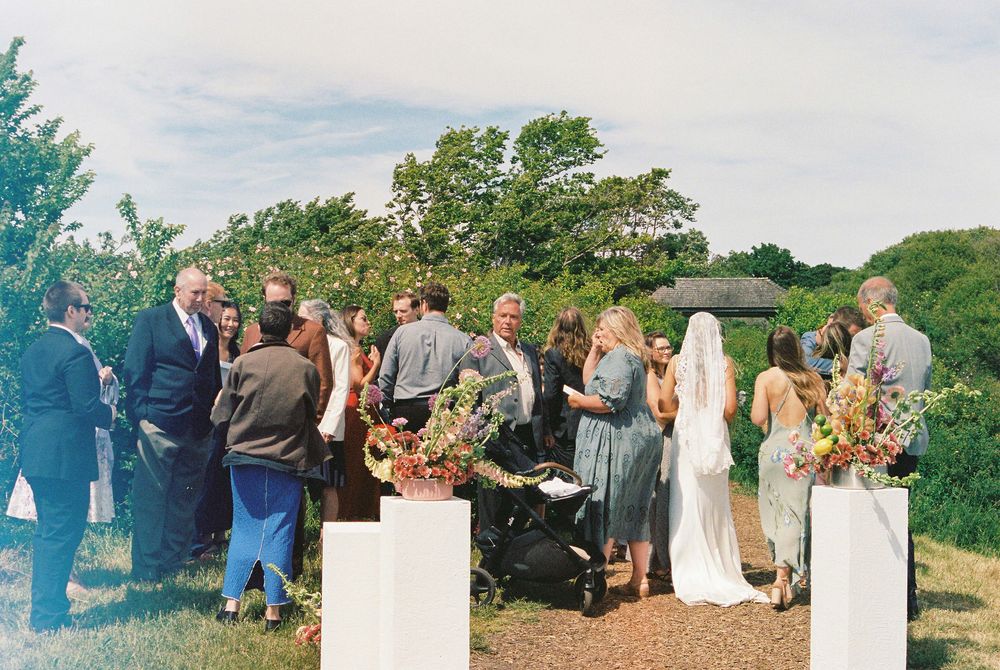 Guests mingle outdoors at an elegant garden wedding ceremony, surrounded by lush greenery and floral arrangements.