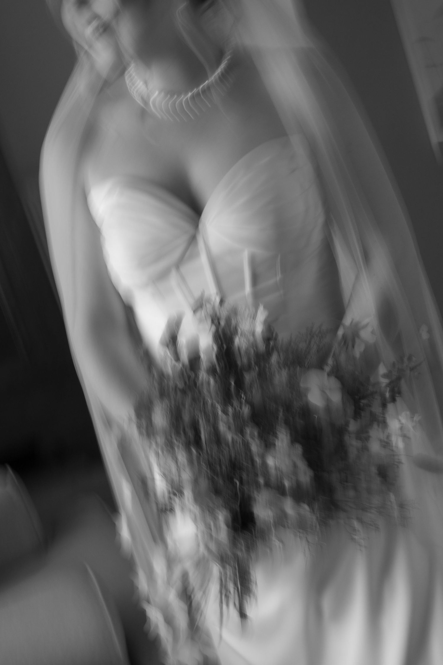 Blurred black and white photo of a bride in a strapless gown holding a wildflower bouquet, wearing a veil and pearl necklace.
