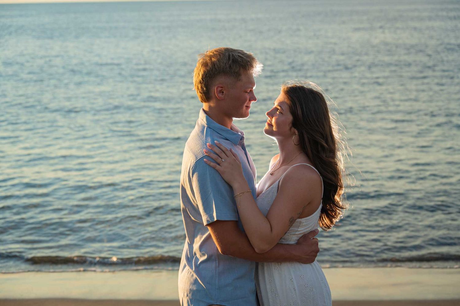 Couple embracing romantically on a beach at sunset with ocean waves in the background.