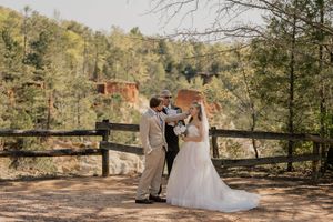 Bride and groom with officiant exchanging vows at outdoor wedding with red clay cliffs backdrop.