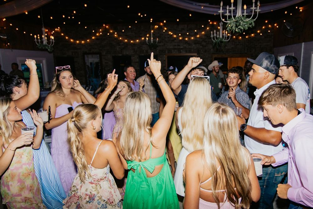 Energetic wedding reception dance floor packed with guests celebrating under warm string lights.