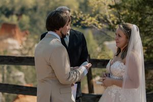 Bride and groom exchange vows outdoors with officiant and scenic autumn backdrop.