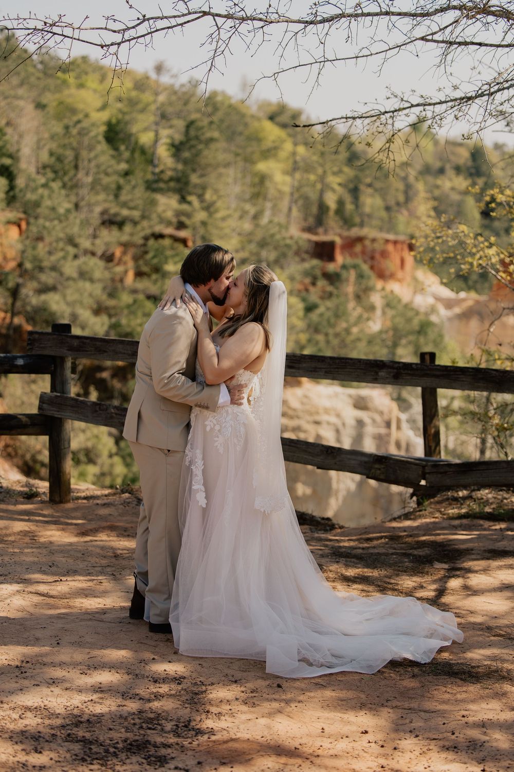 Newlyweds share romantic kiss at scenic overlook with stunning canyon and waterfall views behind them.