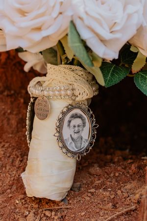Bridal bouquet of white roses with vintage memorial photo charm honoring loved one at wedding.