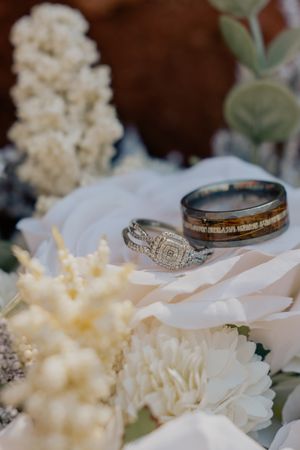 Wedding rings displayed on white florals, featuring diamond halo engagement ring and wood inlay band.
