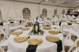 Elegant wedding reception tent with gold charger plates and black ribbon table runners.