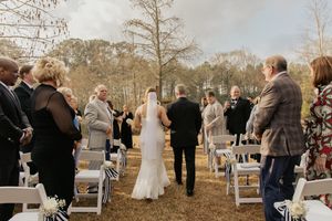 Bride and groom walking down outdoor wedding aisle lined with white chairs and guests.