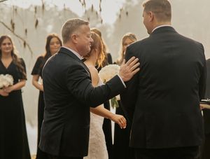 Father of the bride places hand on groom during outdoor wedding ceremony handoff.
