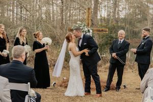 Bride and groom share first kiss at outdoor wedding ceremony with bridesmaids in black dresses.