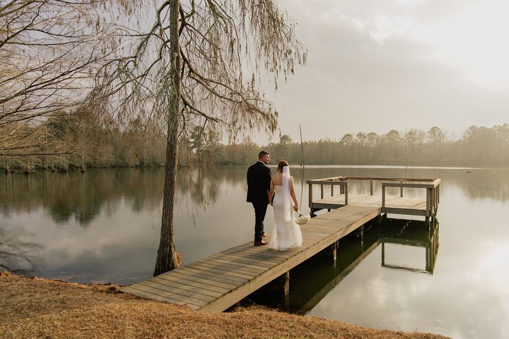 Bride and groom standing on wooden dock overlooking calm misty lake on their wedding day.