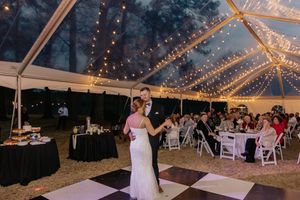 Bride and groom share first dance on checkered floor under string lights in elegant tent reception.
