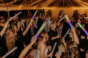 Wedding guests dancing and waving colorful glow sticks under string lights at lively reception party.