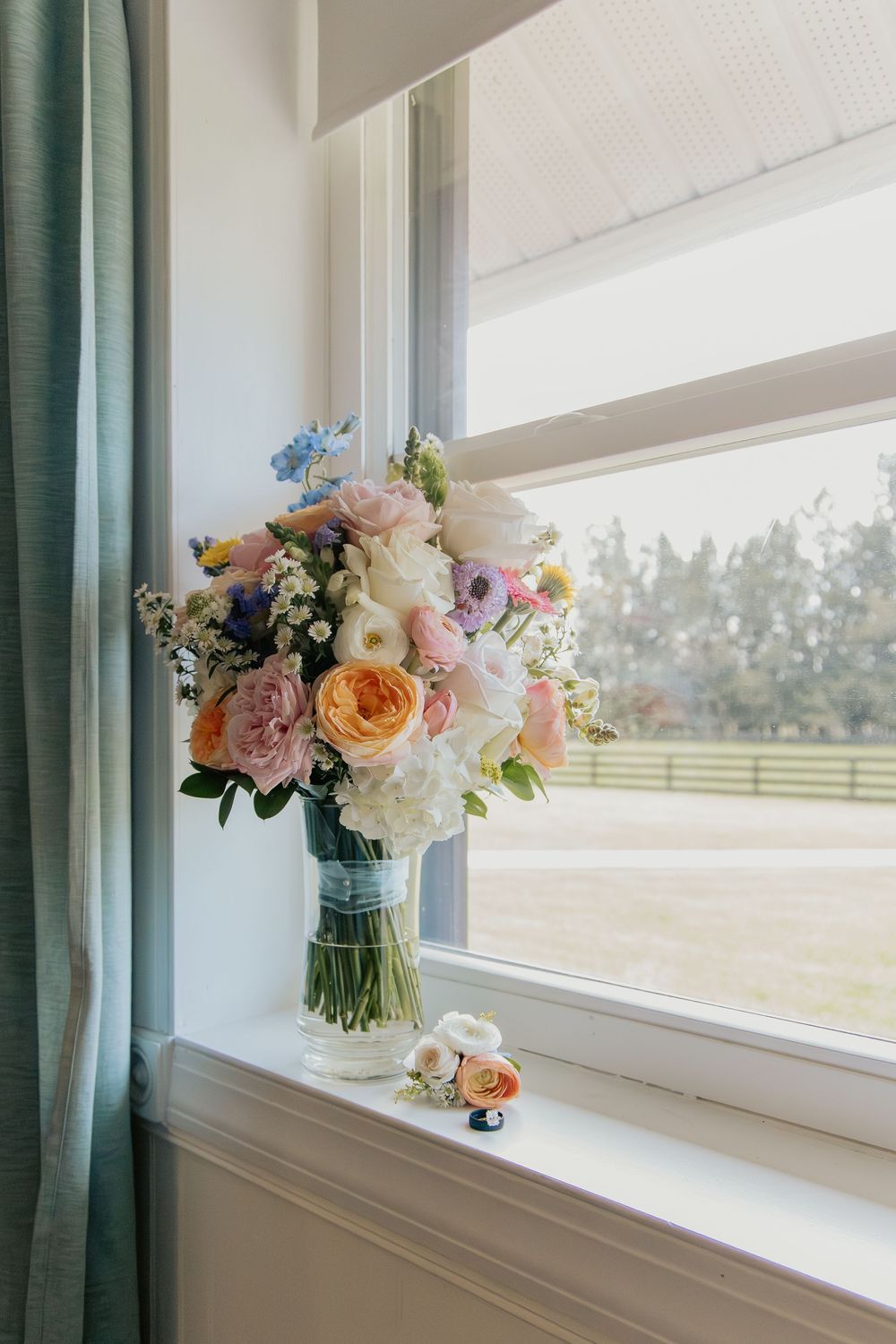Colorful bridal bouquet with peach, pink, and white flowers displayed in a vase on a windowsill.