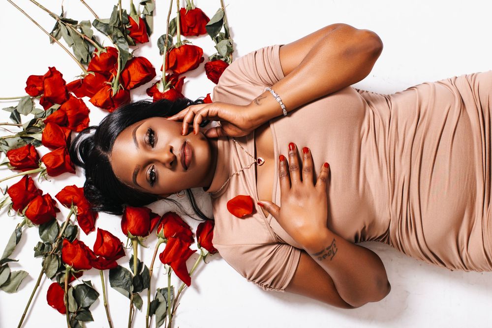 Woman in beige dress lying among red roses on white background, elegant Valentine's Day portrait photography.