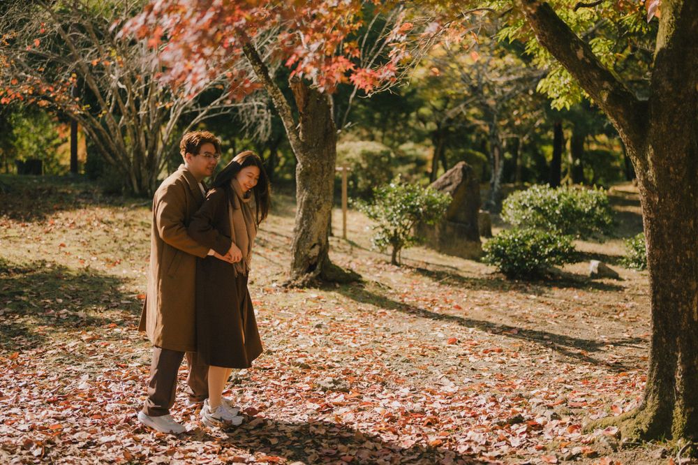 Couple embracing tenderly among vibrant red autumn maple leaves in a serene Japanese garden setting.