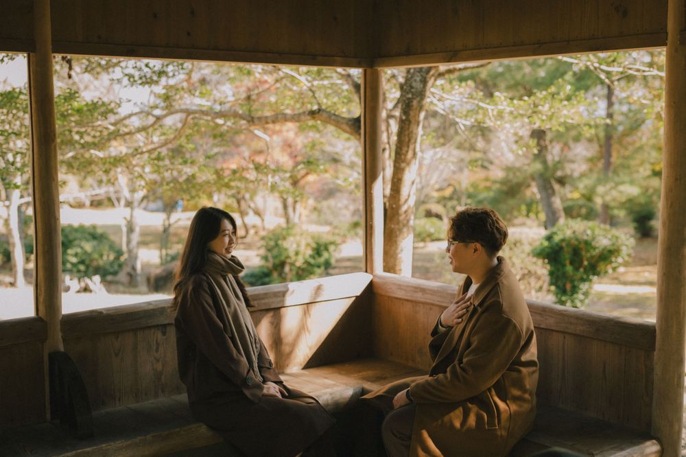 Couple sitting together in a cozy wooden pavilion overlooking a tranquil autumn garden with soft natural light.