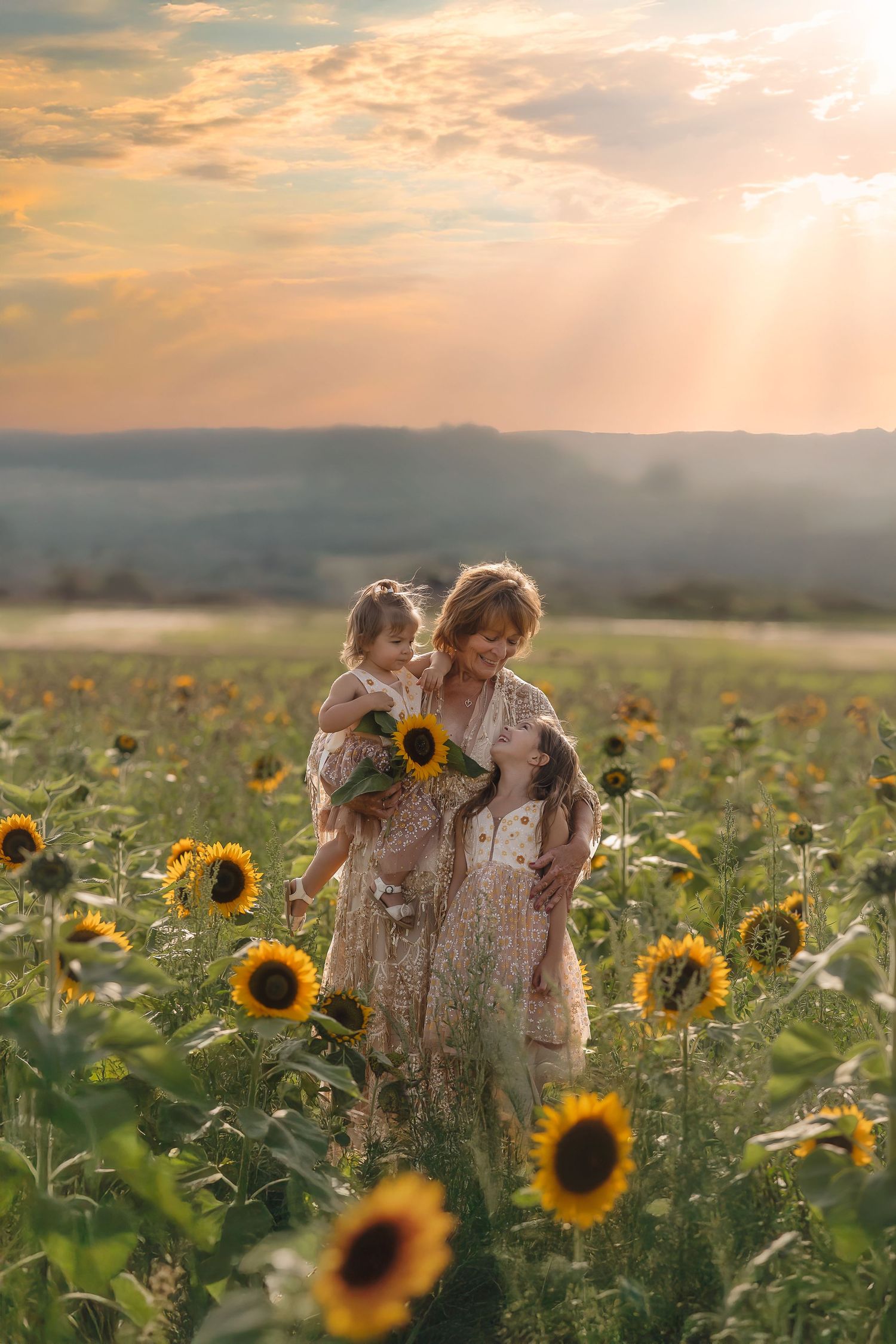 A family walks together through a golden sunflower field at sunset during a maternity photoshoot.