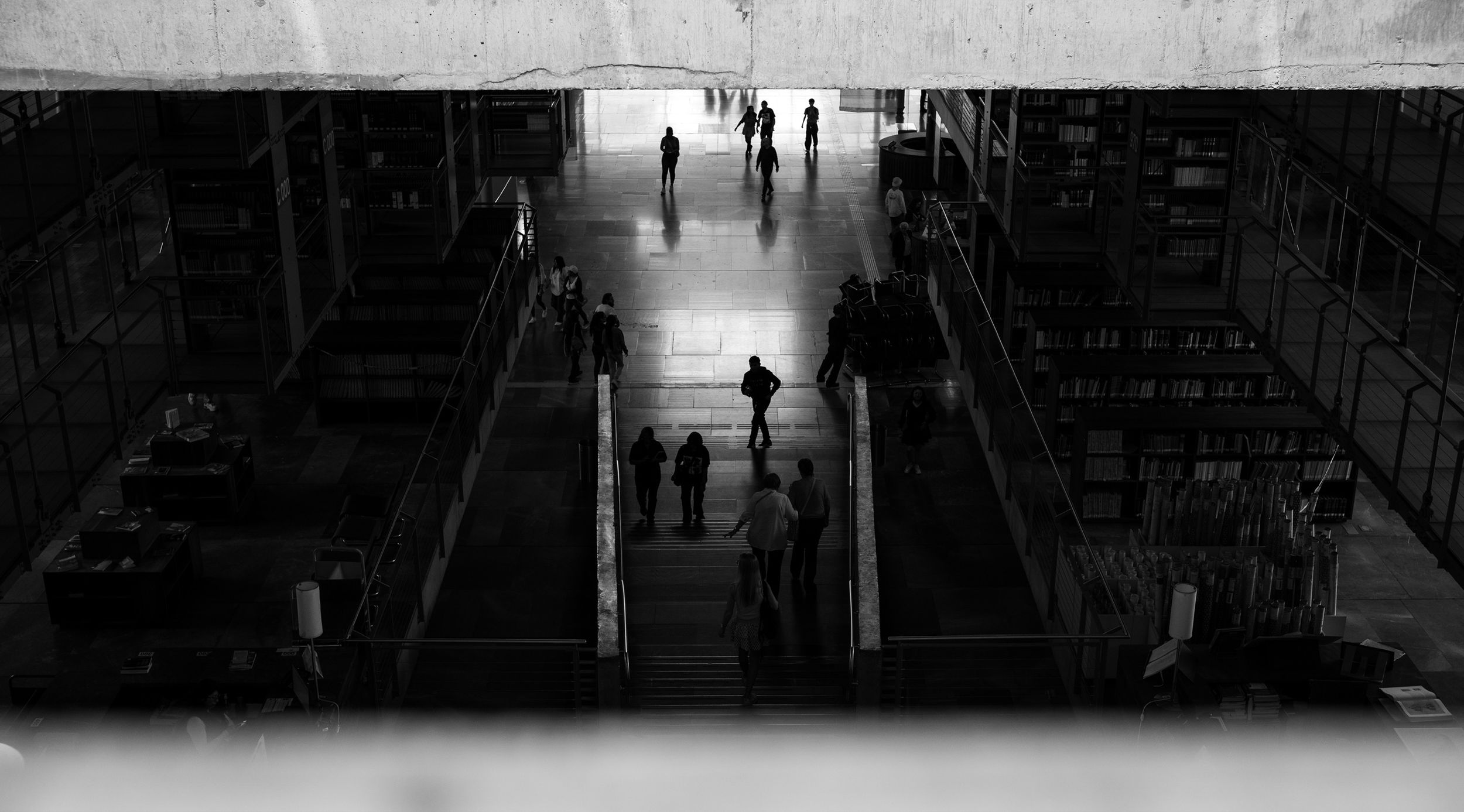 Black and white photo of people walking through a large industrial warehouse with high ceilings and shelving units.