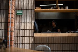 A chef works behind a wooden counter in a modern restaurant with brick walls and open shelving.