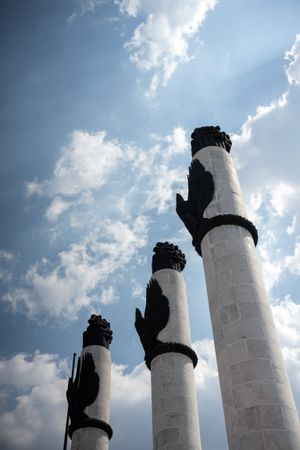 Three tall white stone columns with black eagle sculptures against a dramatic cloudy blue sky.