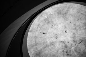Black and white architectural photo of a circular skylight with curved concrete walls creating geometric patterns.