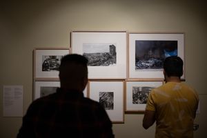 Two visitors view framed black-and-white photography prints displayed on a gallery wall in a museum exhibition.