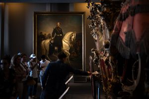 Museum visitors viewing a large equestrian portrait painting displayed in a dimly lit gallery with ornate artifacts.