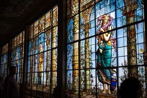 Stunning stained glass windows depicting classical figures in vibrant colors illuminate a grand historic building interior.