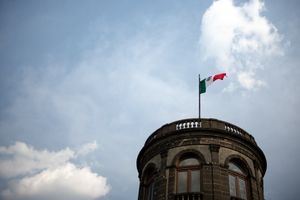 Historic stone tower with Mexican flag waving against a cloudy blue sky.