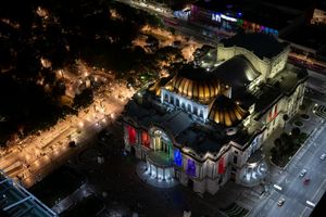 Aerial night view of Palacio de Bellas Artes in Mexico City, illuminated with colorful lights against dark streets.