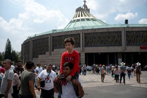 A boy sits on a man's shoulders in front of the Basilica of Guadalupe in Mexico City, surrounded by crowds.