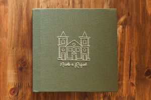 Green linen wedding photo album with gold embossed church illustration and couple names on wooden surface.