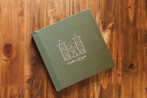 Green linen wedding album with embossed church illustration and couple names on rustic wooden surface.