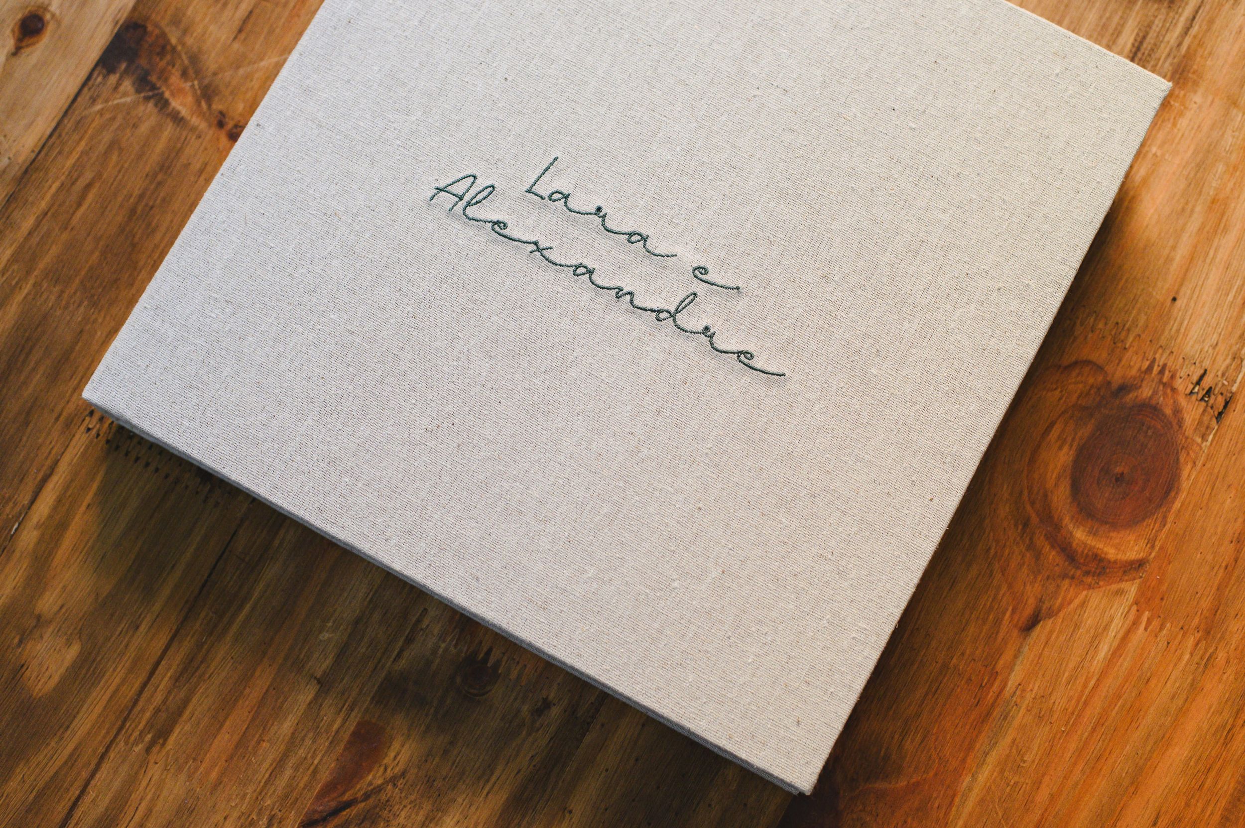 Elegant linen-covered wedding album with silver embossed script names on a rustic wooden surface.