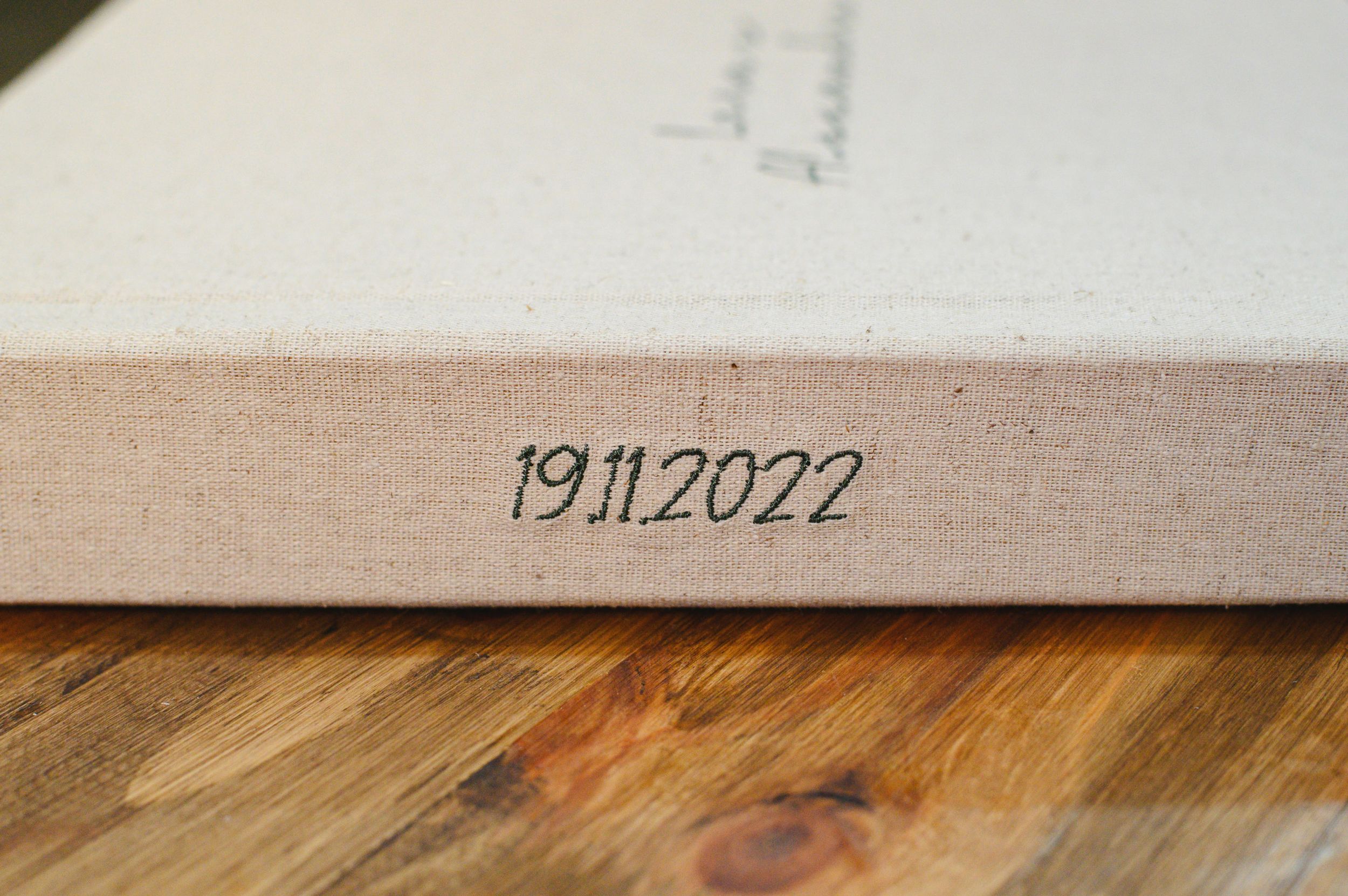 Beige linen photo album spine stamped with date 19.11.2022 resting on a wooden surface.