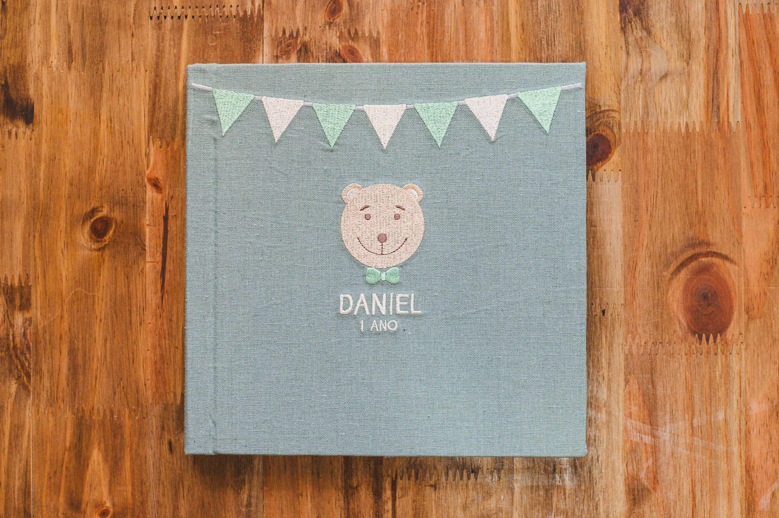 Personalized baby memory book with bear design, mint bunting, and name Daniel embroidered on gray fabric cover.