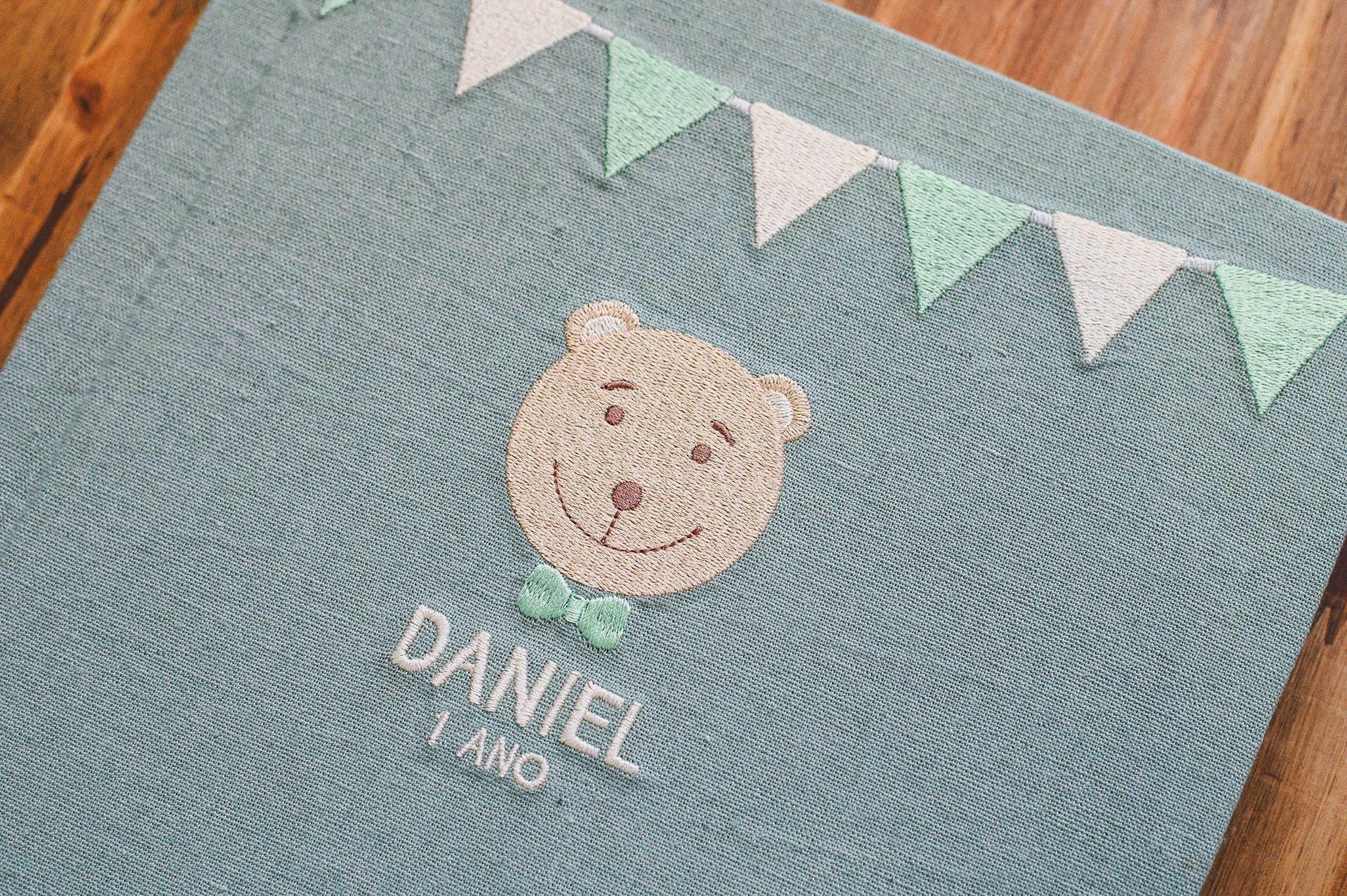 Teal linen baby photo album embroidered with a teddy bear and name Daniel 1 Ano, decorated with fabric bunting.