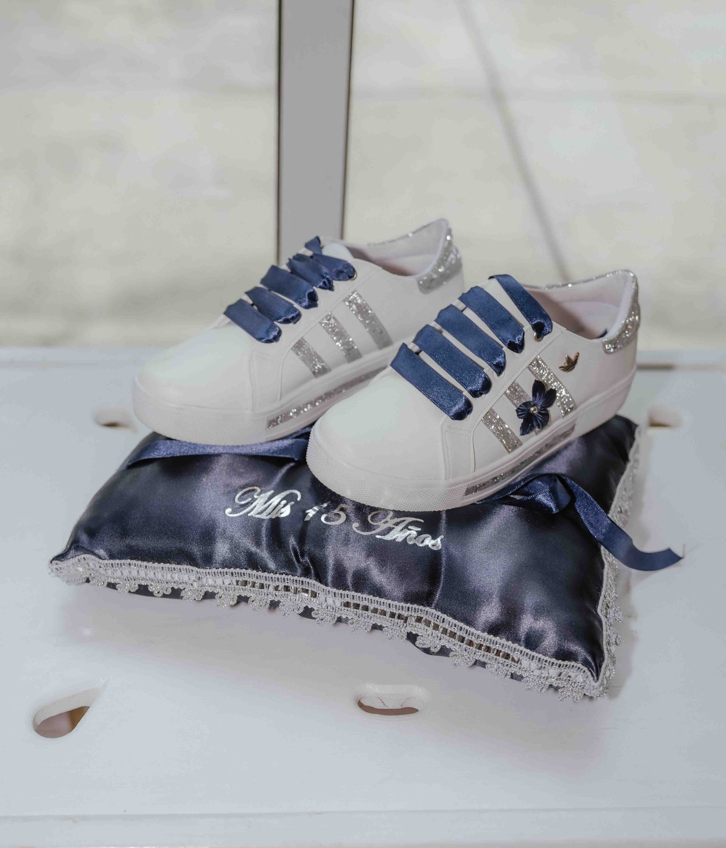 White sneakers with navy blue laces and floral details displayed on a satin Mr & Mrs wedding ring pillow.