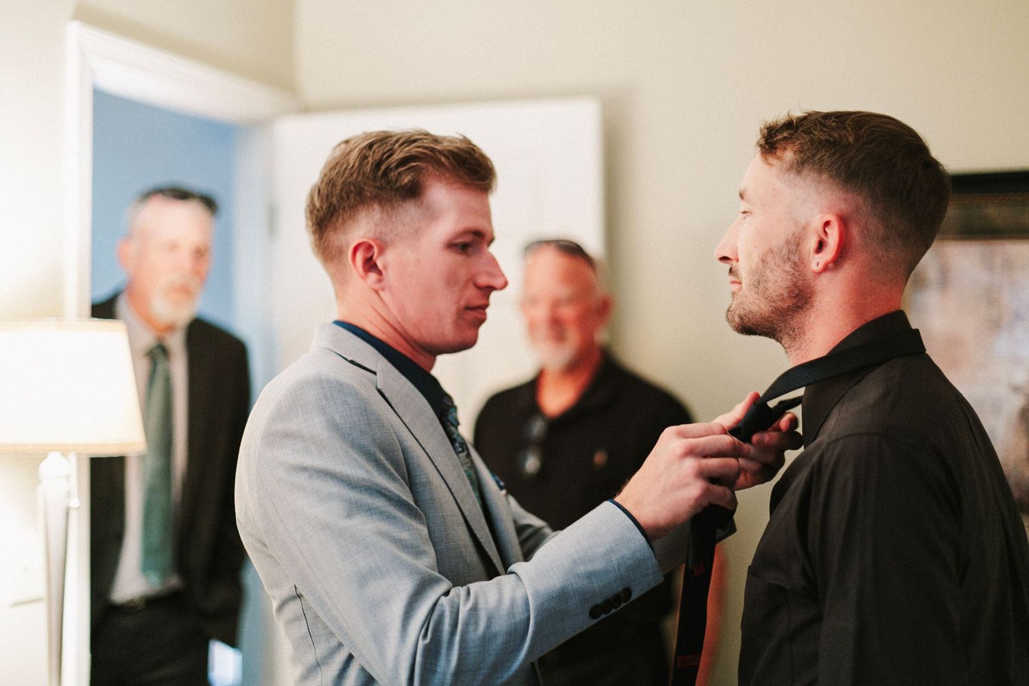 Groomsmen helping each other with tie adjustments before a wedding ceremony indoors.