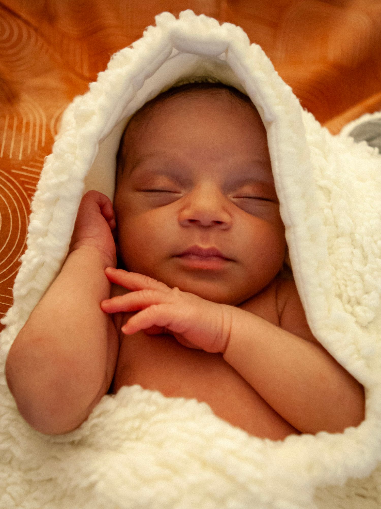 Peaceful newborn baby sleeping wrapped in a soft white fluffy blanket with tiny hands visible near face.