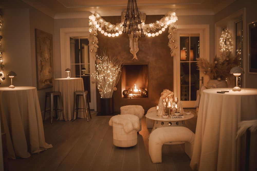 Cozy elegant event lounge with warm fireplace, string lights, white plush seating, and romantic candlelit ambiance.